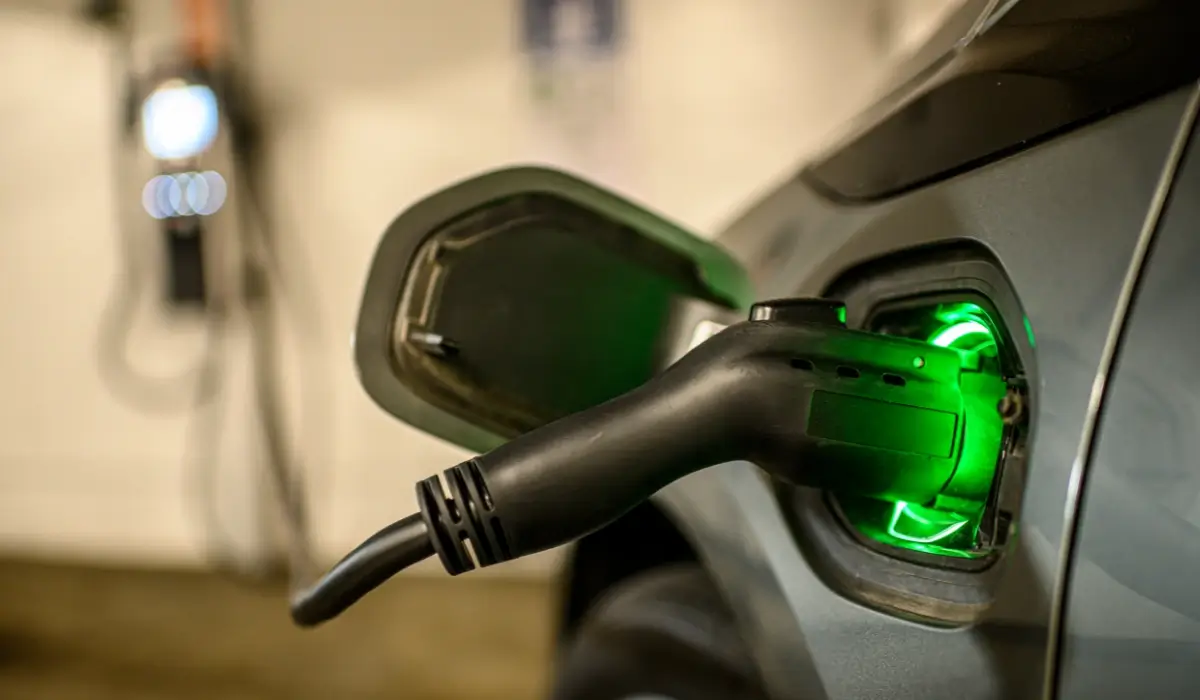 EV charging connector locked into a vehicle charge port with a green indicator light in a parking garage