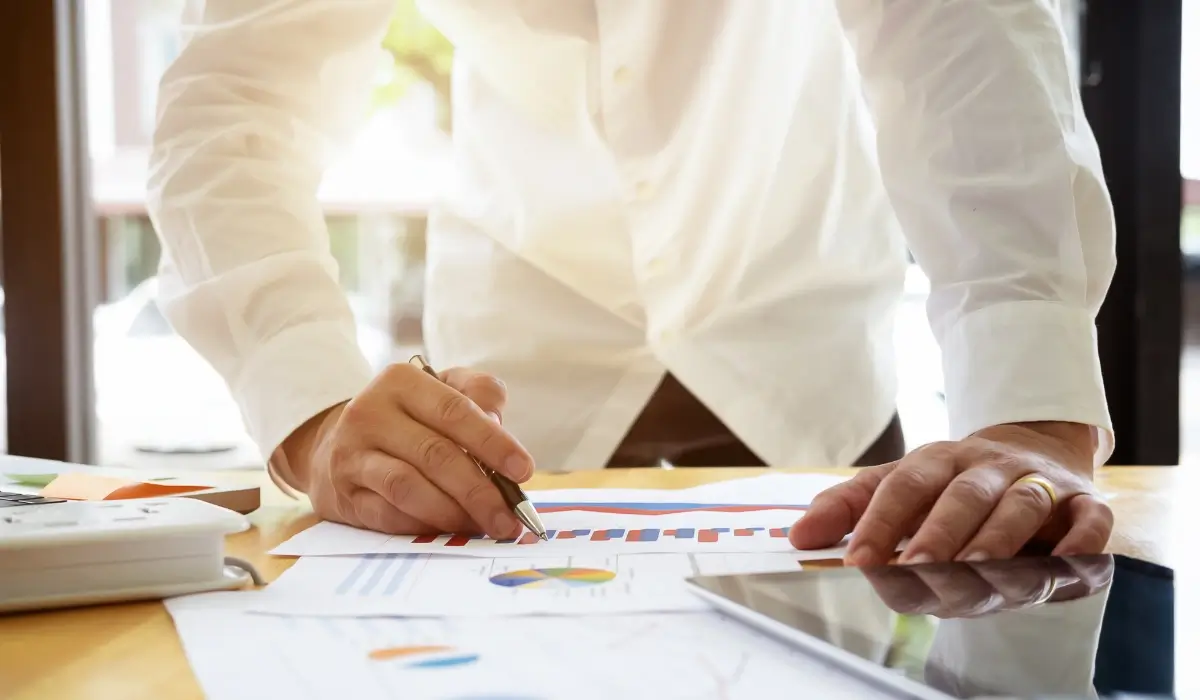 Business professional reviewing charts and planning documents at a desk with a tablet. Image 2: