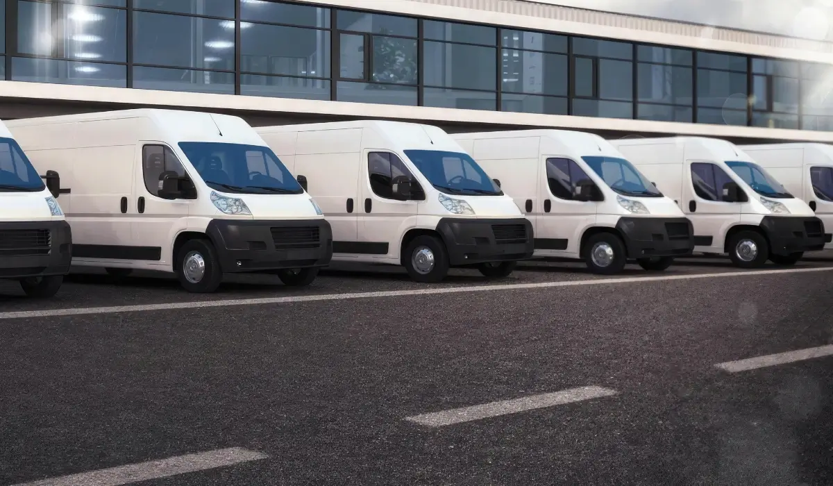 Row of white commercial delivery vans parked outside a fleet facility.