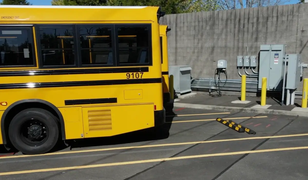 Yellow school bus parked beside electric vehicle charging equipment at a depot
