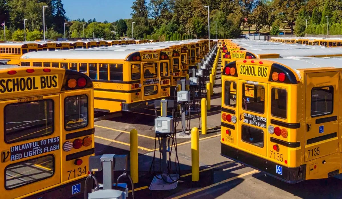 Multiple school buses parked at a depot with rows of electric bus charging stations