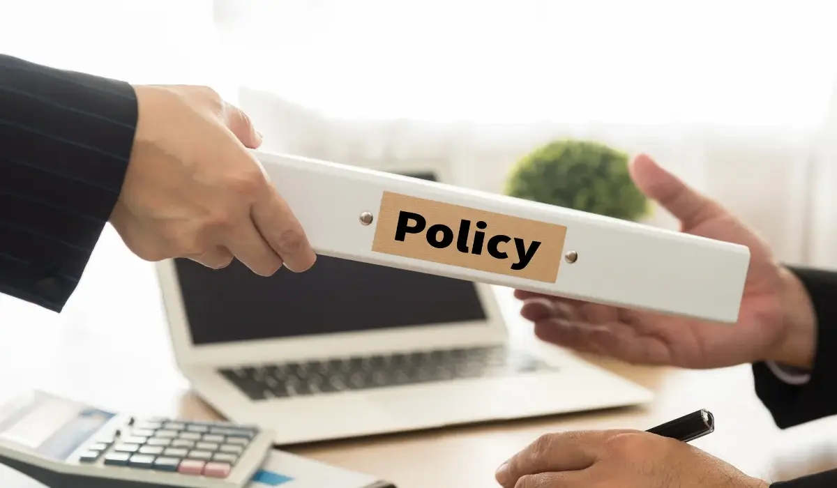Business professionals exchanging a document labeled Policy in an office setting.