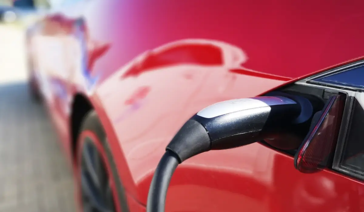 Close-up of a black and silver charging connector plugged into the charge port of a glossy red electric car.