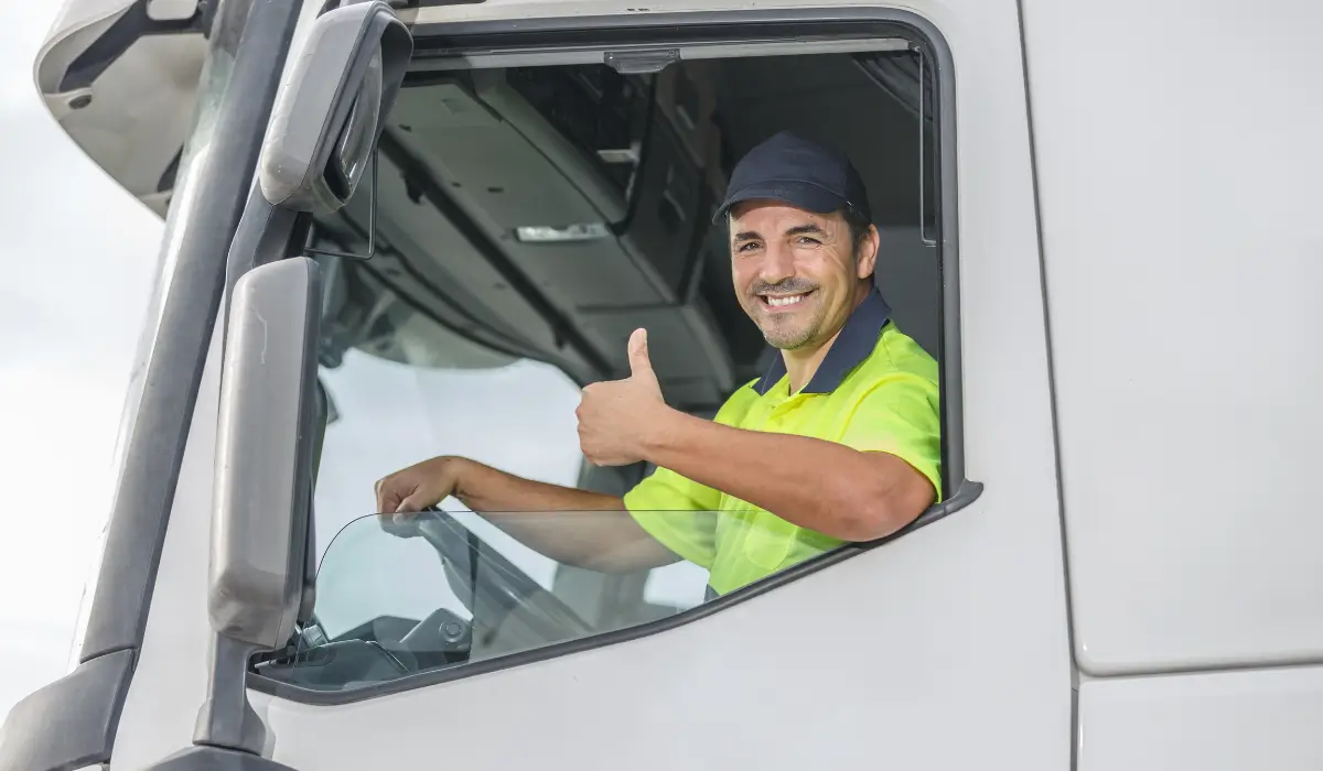 Truck driver giving a thumbs-up from the cab of a commercial truck.