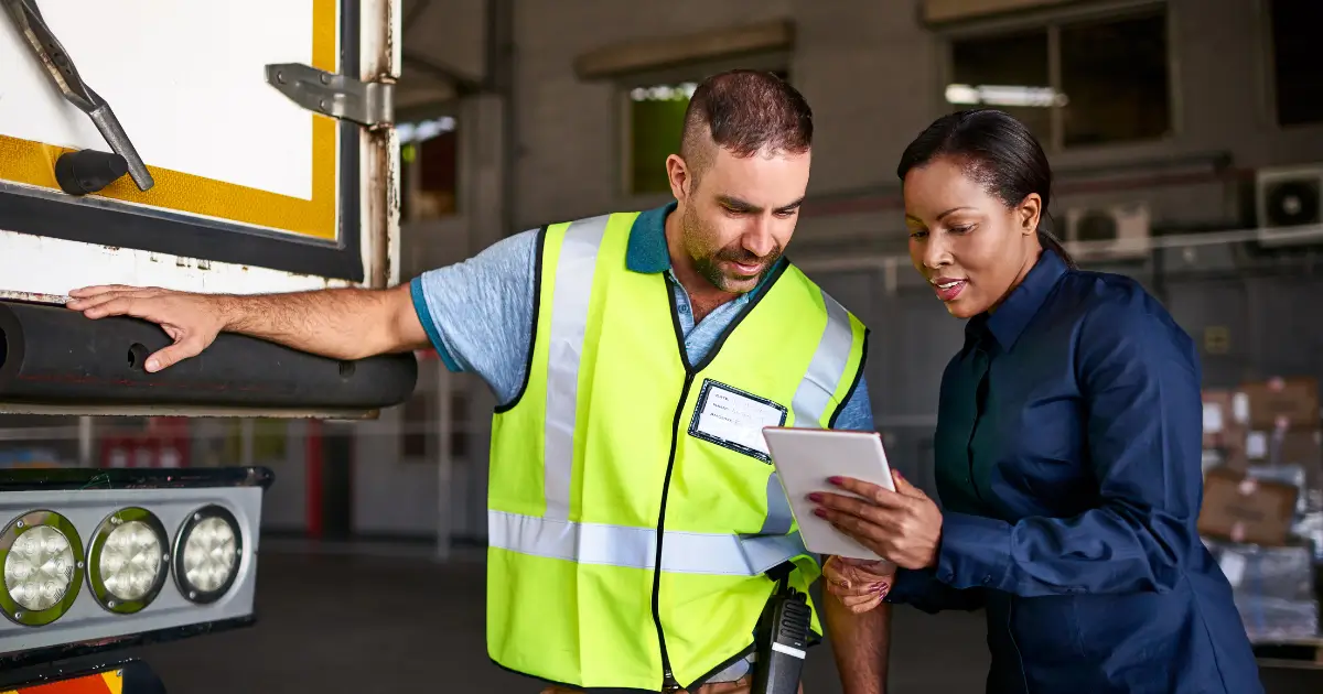 Fleet manager and depot worker reviewing EV charging data on a tablet beside a truck