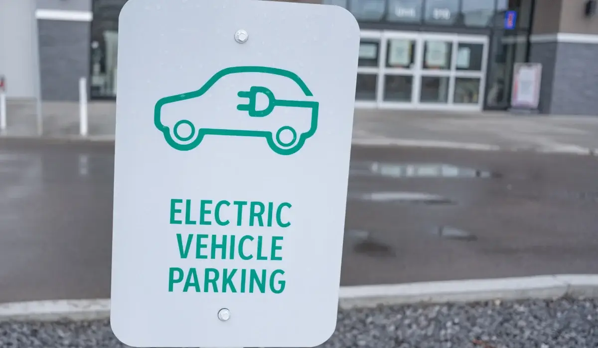 Electric vehicle parking sign with a green car and charging plug symbol outside a building.